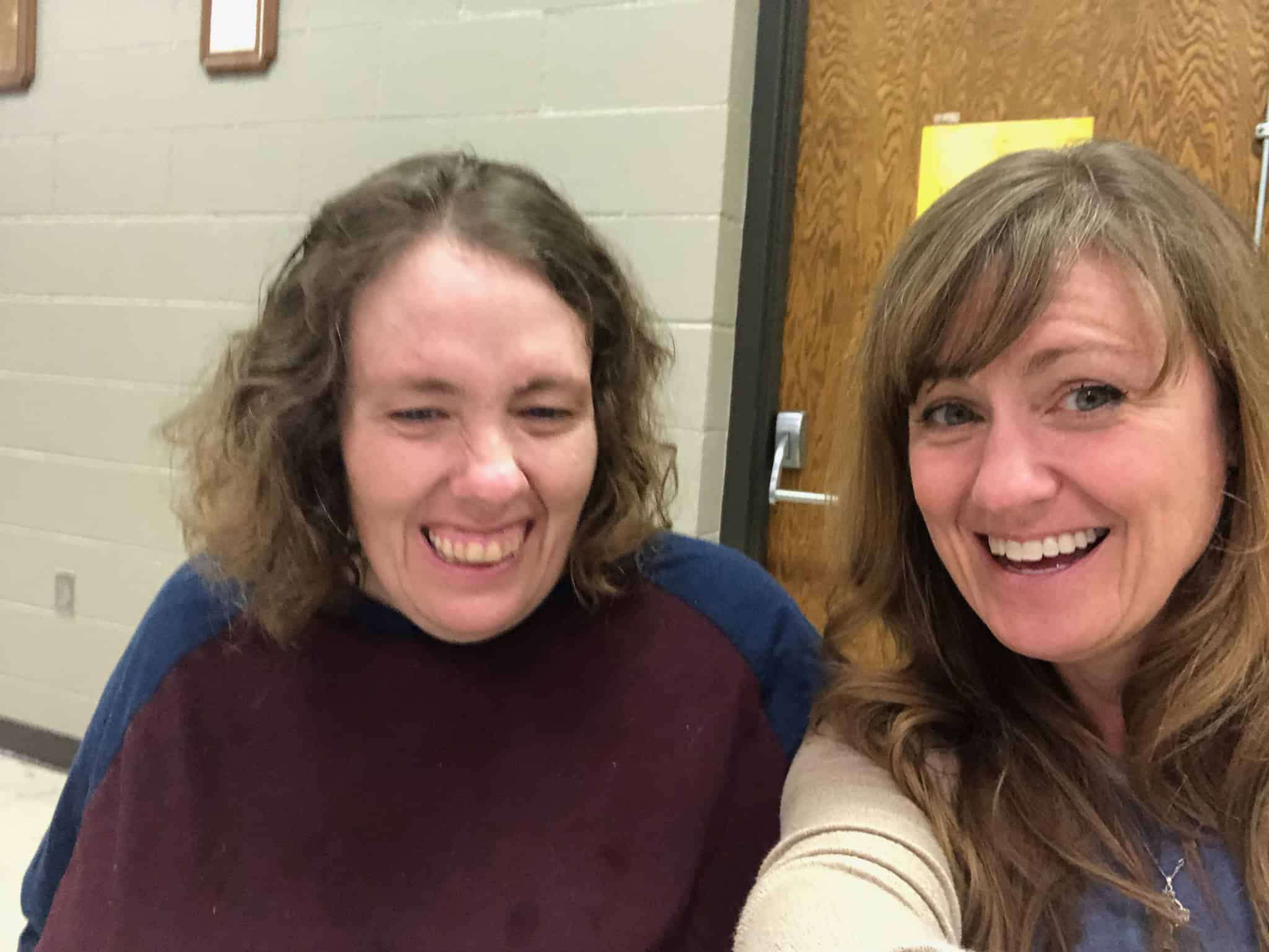 Two women smiling and taking a selfie in an indoor setting.