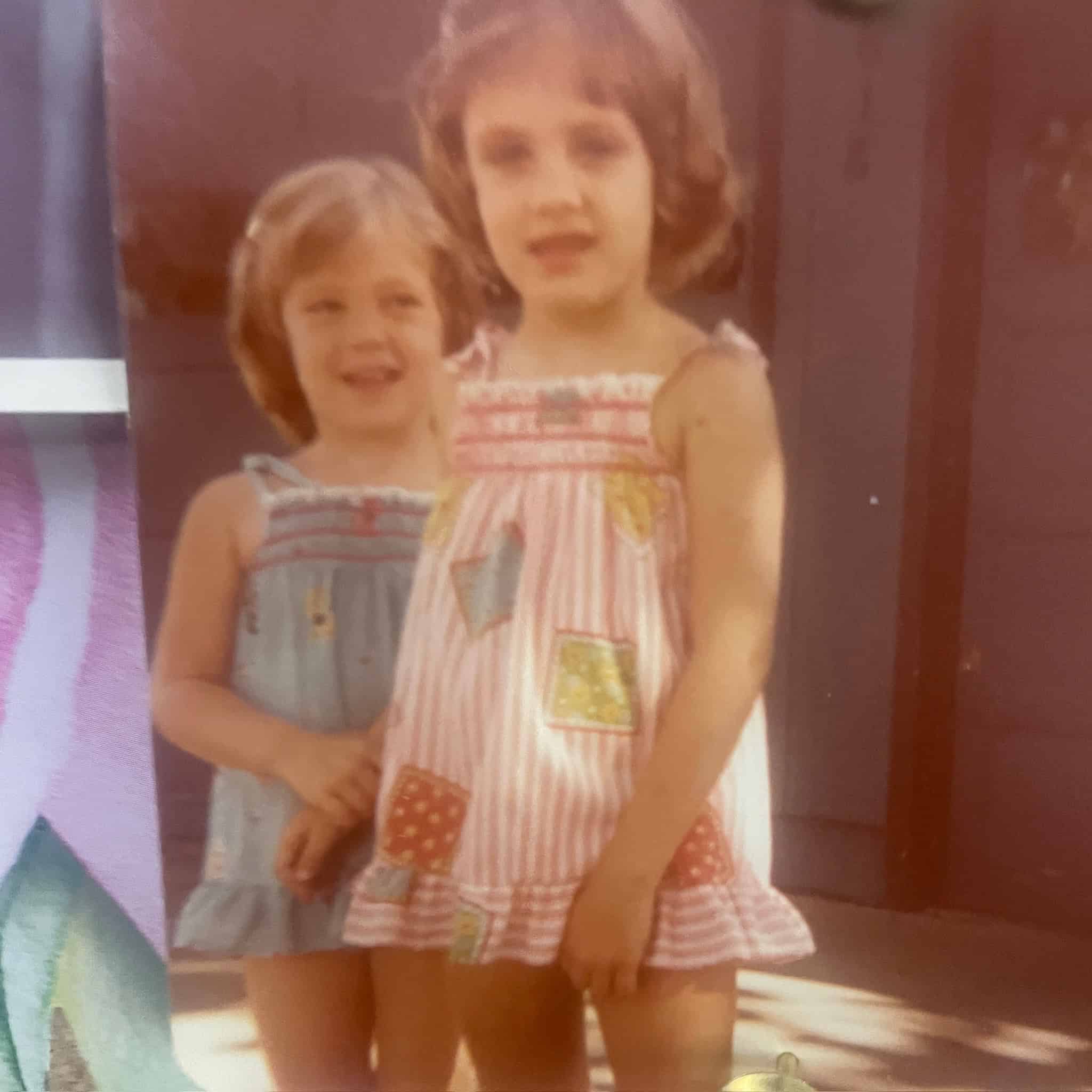Two young girls standing outdoors, smiling and enjoying a sunny day.