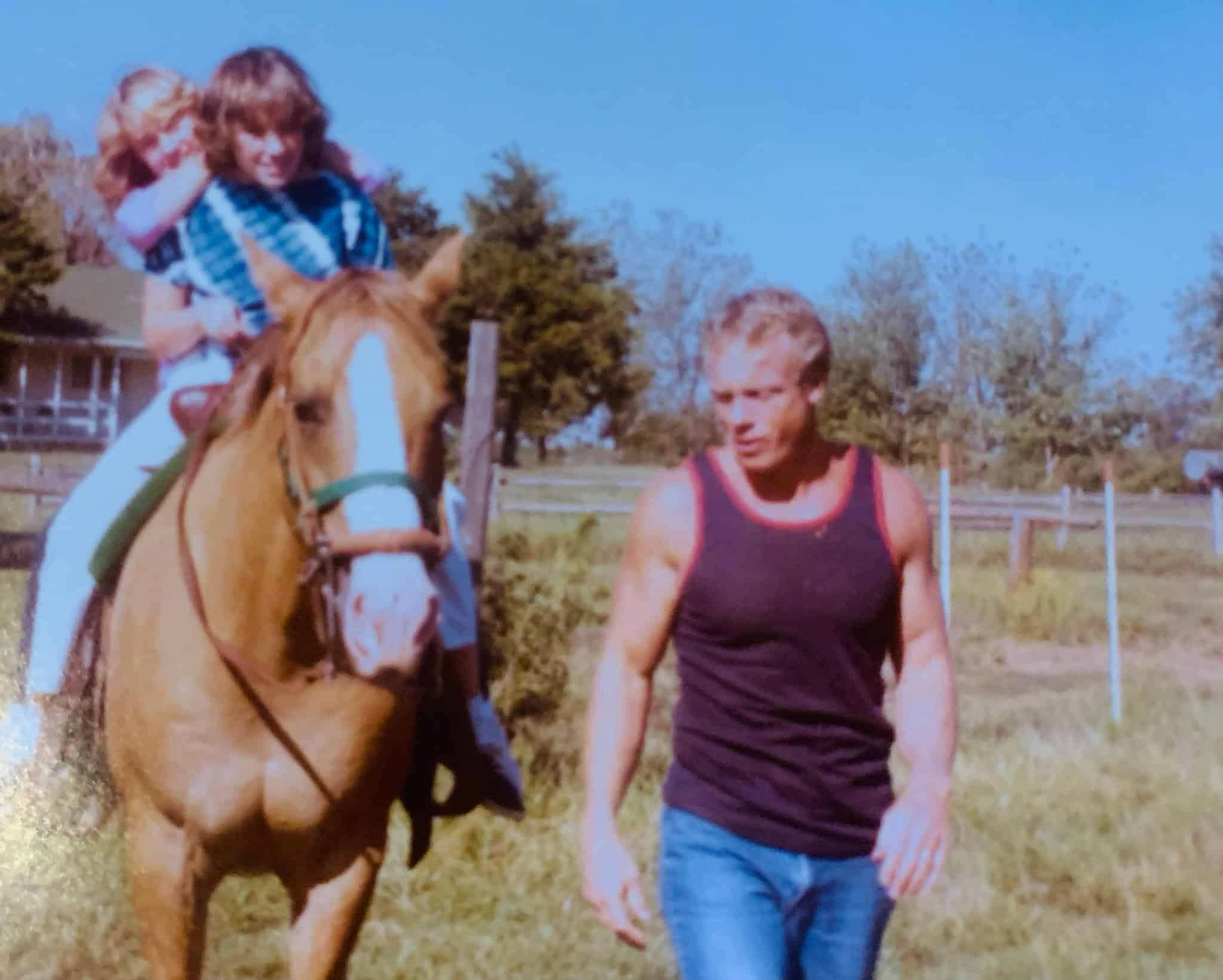 Child riding a horse with an adult walking nearby outdoors on a sunny day.