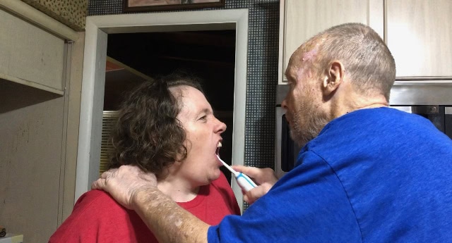 Person administering a throat swab to another person in a home setting.