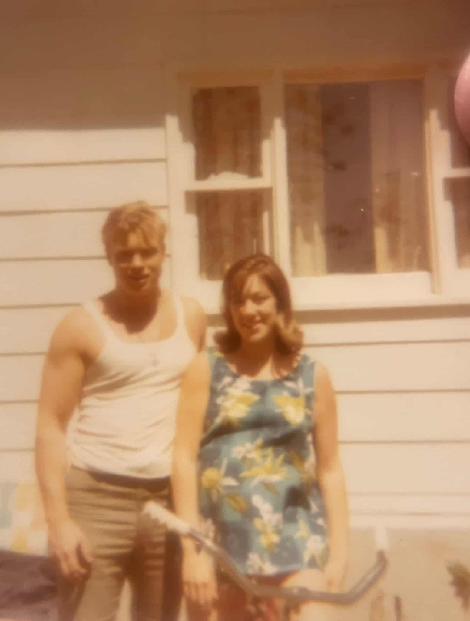 Two people standing outside a white house with a window in the background.