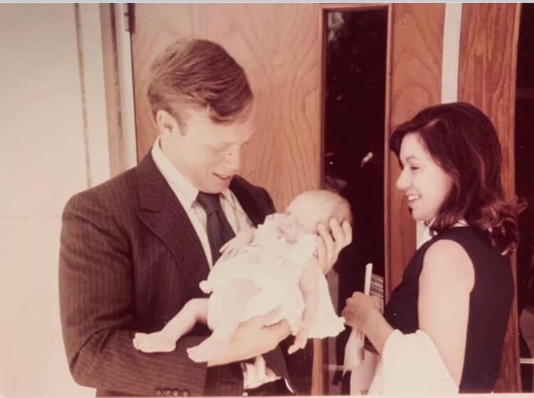 Man and woman smiling at a baby in a warm indoor setting.