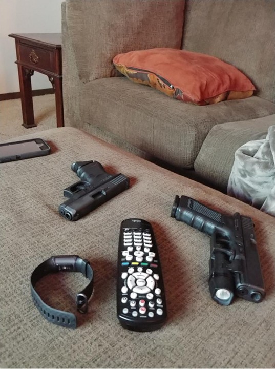 Two handguns, a phone, a watch, and a TV remote laid out on a coffee table